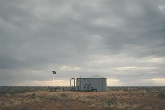 A small water pump station and steel tank standing alone in dry Australian rangeland under an overcast sky.